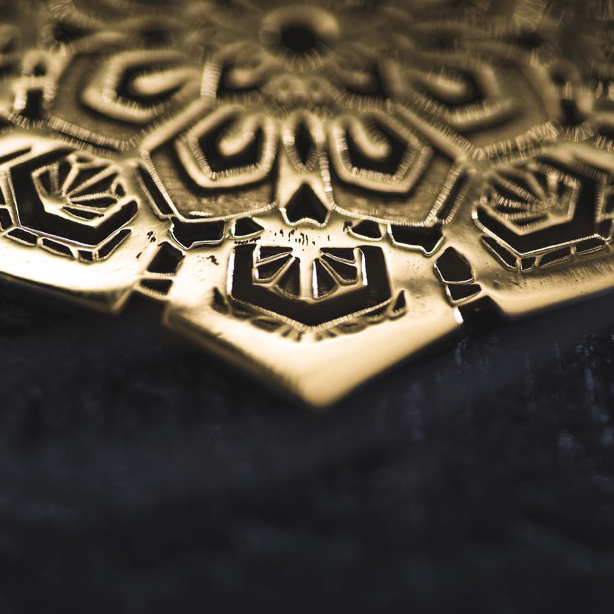 A close-up image of the ASA Oversized Asa No Ha Mandala Disc Earrings in Gold by Kaya Movement, showcasing an intricate geometric and floral design reminiscent of ethnic statement jewelry. The lighting highlights the depth and detail of the 16 gauge etched metal, accentuating its metallic sheen against a dark background.
